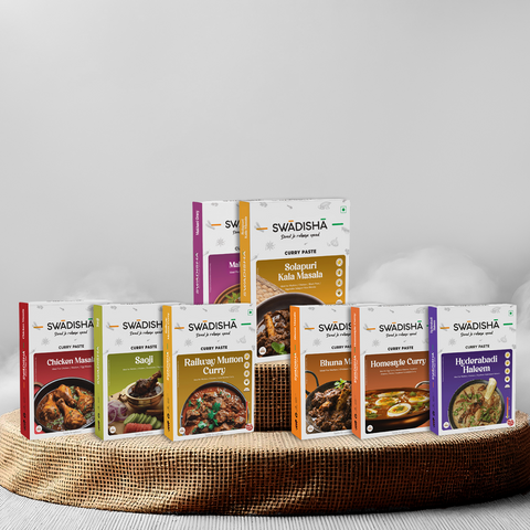 A collection of eight packaged food items from Swadisha, including various Ready to cook curry pastes and spices, displayed on a woven mat against a white background.